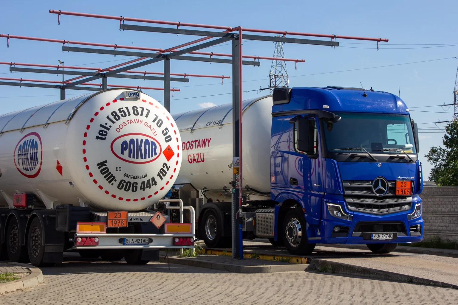 Autocysterny PAKAR przy instalacji przeładunkowej terminala LPG: tył naczepy-cysterny z logo i numerem telefonu, obok niebieski ciągnik Mercedes-Benz Actros